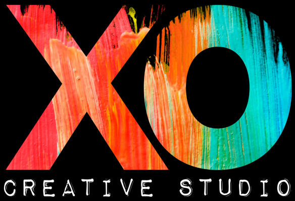Logo for Xan's company, XO Creative Studio. The letters X and O appear in painted streaks of coral, orange, and teal. Below that, the words "Creative Studio" appear in small white text, using a font that looks printed or pressed, like a typewriter or a lab